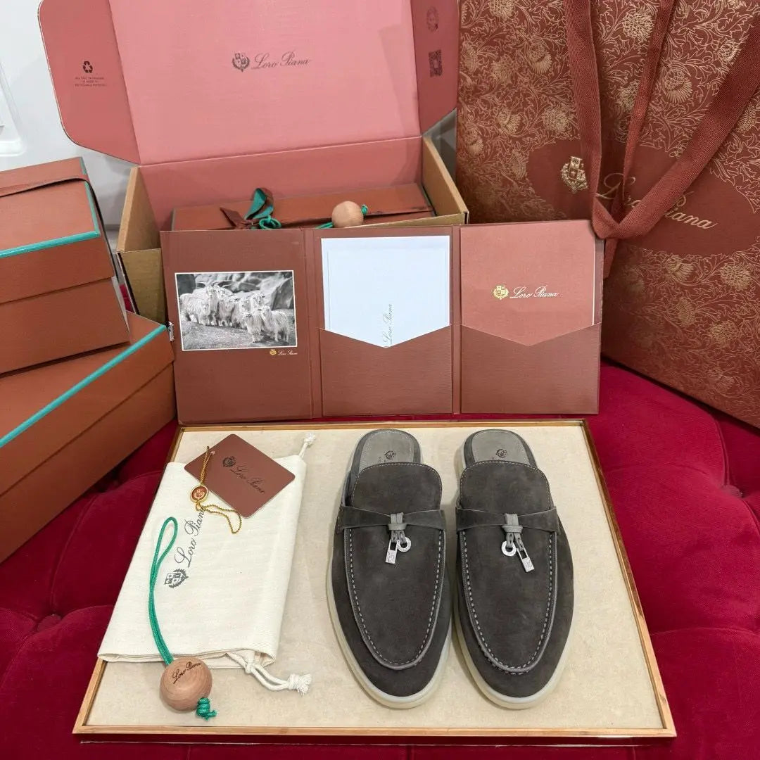 A pair of brown suede Sea-Sail Walk Loafer shoes with lace-up closure, displayed in their packaging, which includes a box and a pocket-like structure with a picture and a paper inside. The shoes are placed on a white surface with a decorative red and white item to the side.